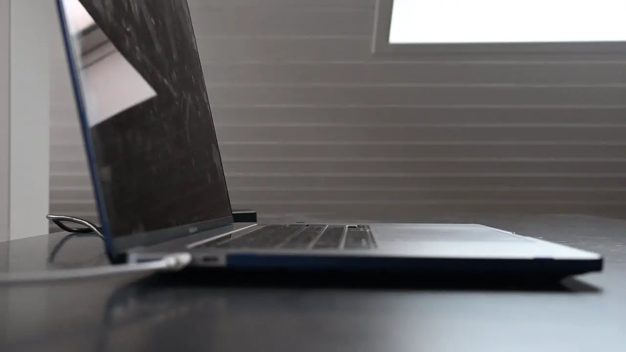 Side view of a laptop on a desk with the keyboard and a white cable plugged in to charge