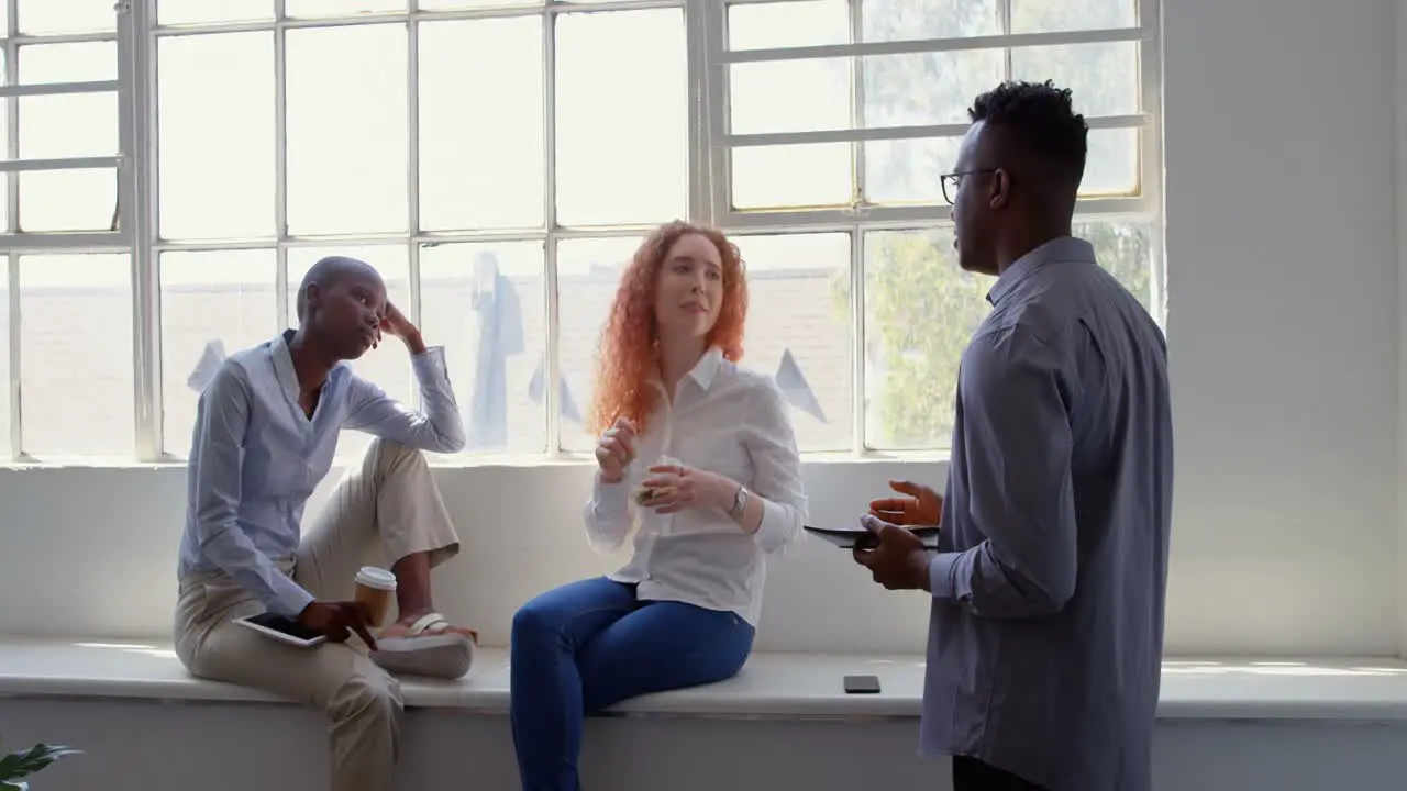 Front view of young mixed-race business team eating food and drinking coffee in modern office 4k