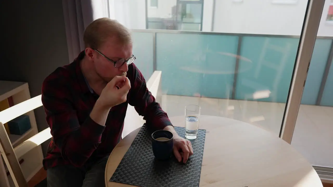 Young Man Sits at Table and Drinks Coffee Stirs it with Spoon Lazy Day at Home