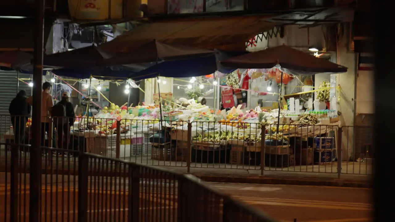 Static shot of people walking through a local fruit and vegetable shop and a bus appearing in view