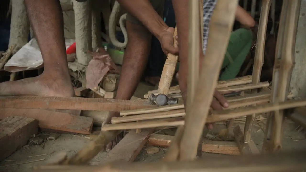 Unrecognized poor labour hammering nails on bamboo stick