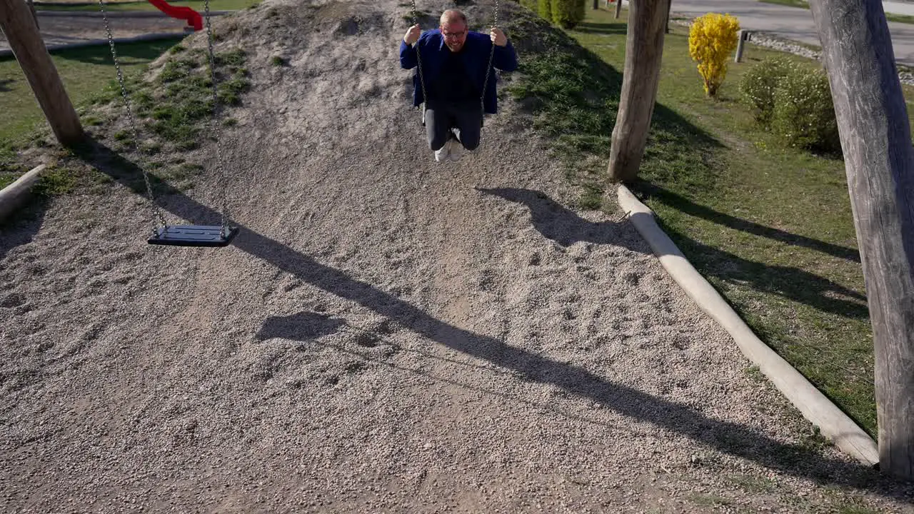 Adult Man Smiles Enjoys Swings in Park Slow Motion on Sunny Day