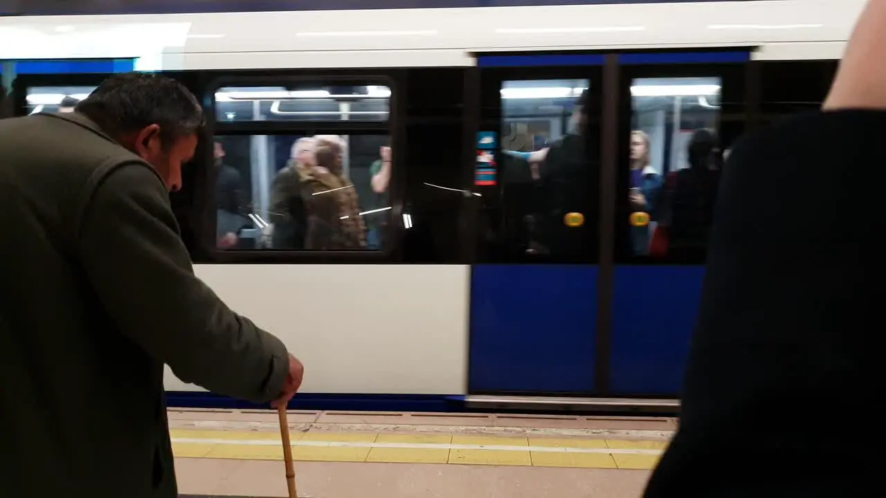 Metro train arrive in Madrid city underground station people waiting on the subway platform Old man with crutch enters frame from the left