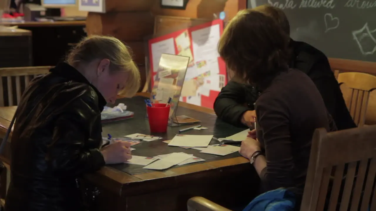 A small group of people writing letters to Santa Claus sit at a table in Santa Claus Village in Finland