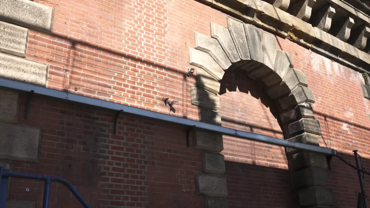 Static shot of a brick wall with moving shadows of people moving through the frame