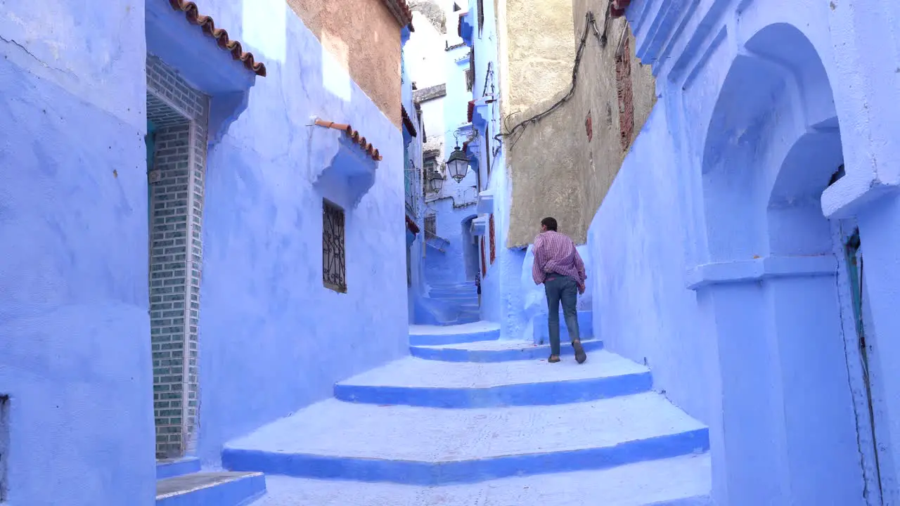 A man walking up the blue stairs in Chefchaouen the blue city of Morocco