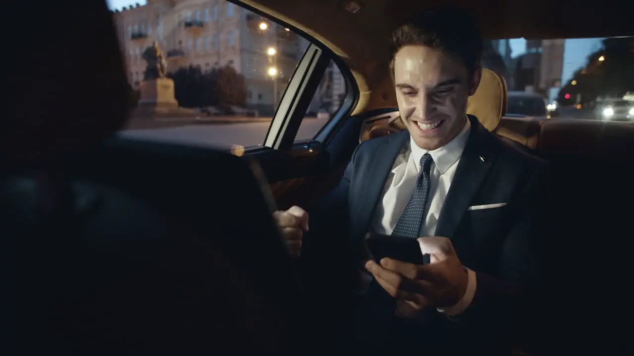 Excited business man rejoicing from good news on smartphone in luxury car