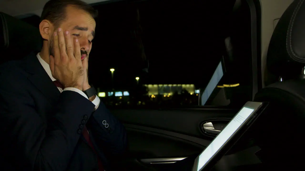 Businessman working at night on his laptop from the back seat of his luxury car