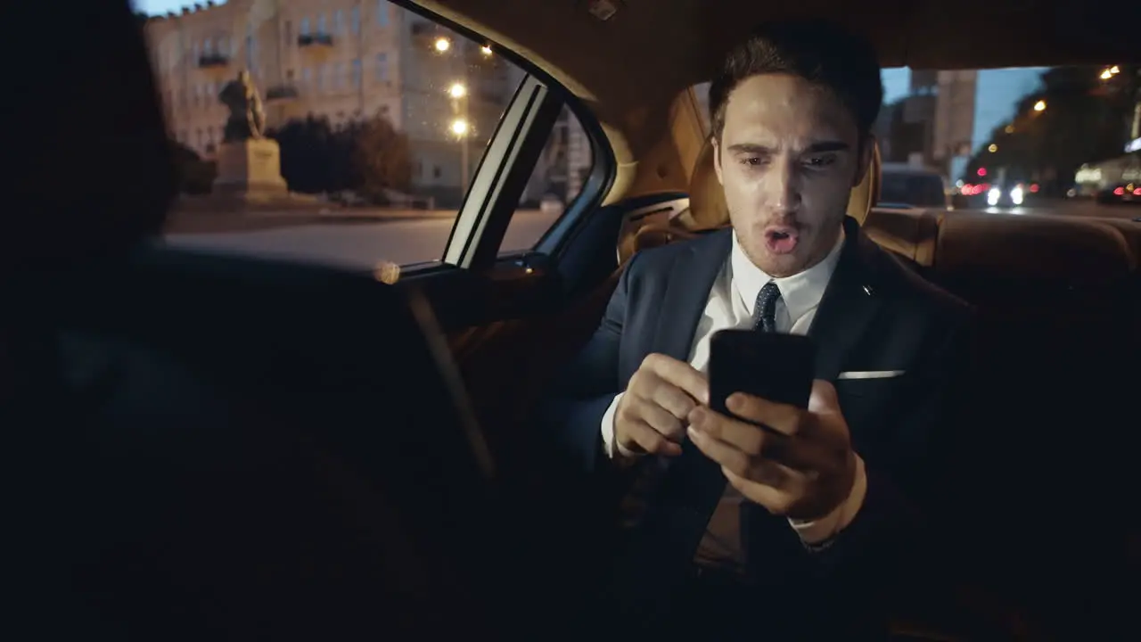 Annoyed business man swearing on video chat on smartphone in dark car