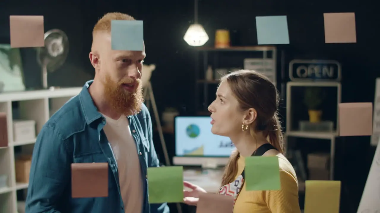 Young business partners discussing ideas on sticker board in hipster office