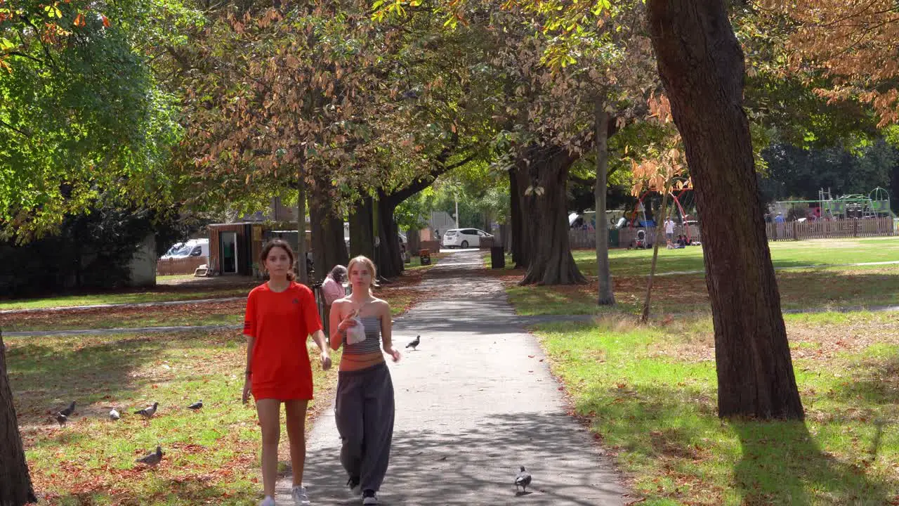 A couple of young girls walking through Wanstead green shaded by the trees