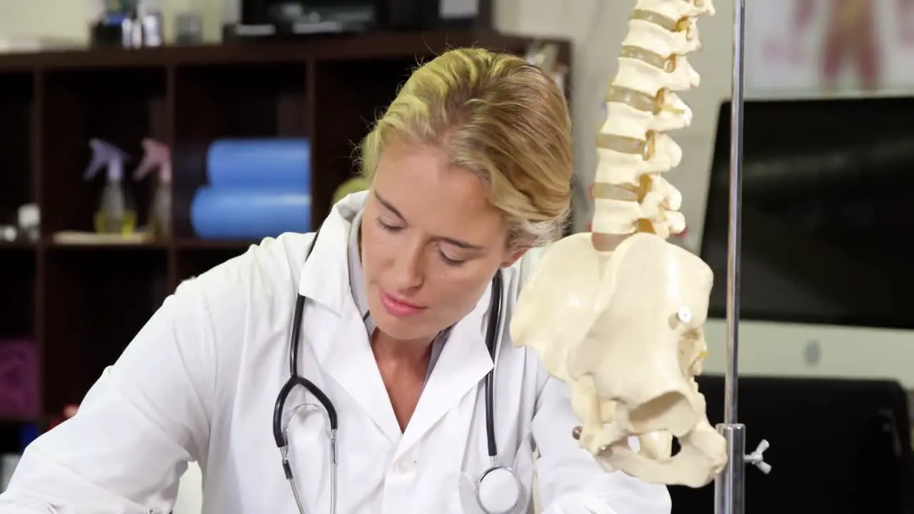 Physiotherapist looking at spine model while writing on clipboard