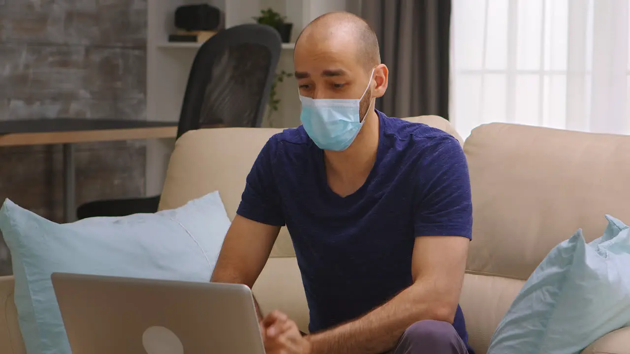 Man wearing mask waving at laptop screen