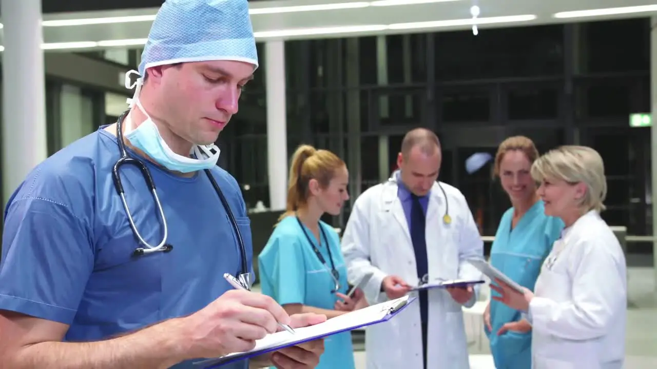 Smiling surgeon writing on clipboard in hospital corridor