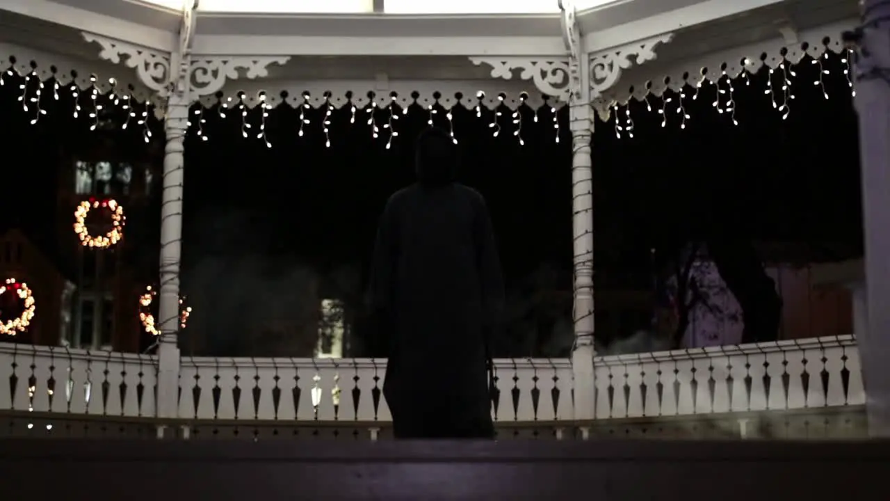 Tilt up WIDE-SHOT of someone in a Grim Reaper costume in front of Christmas lights