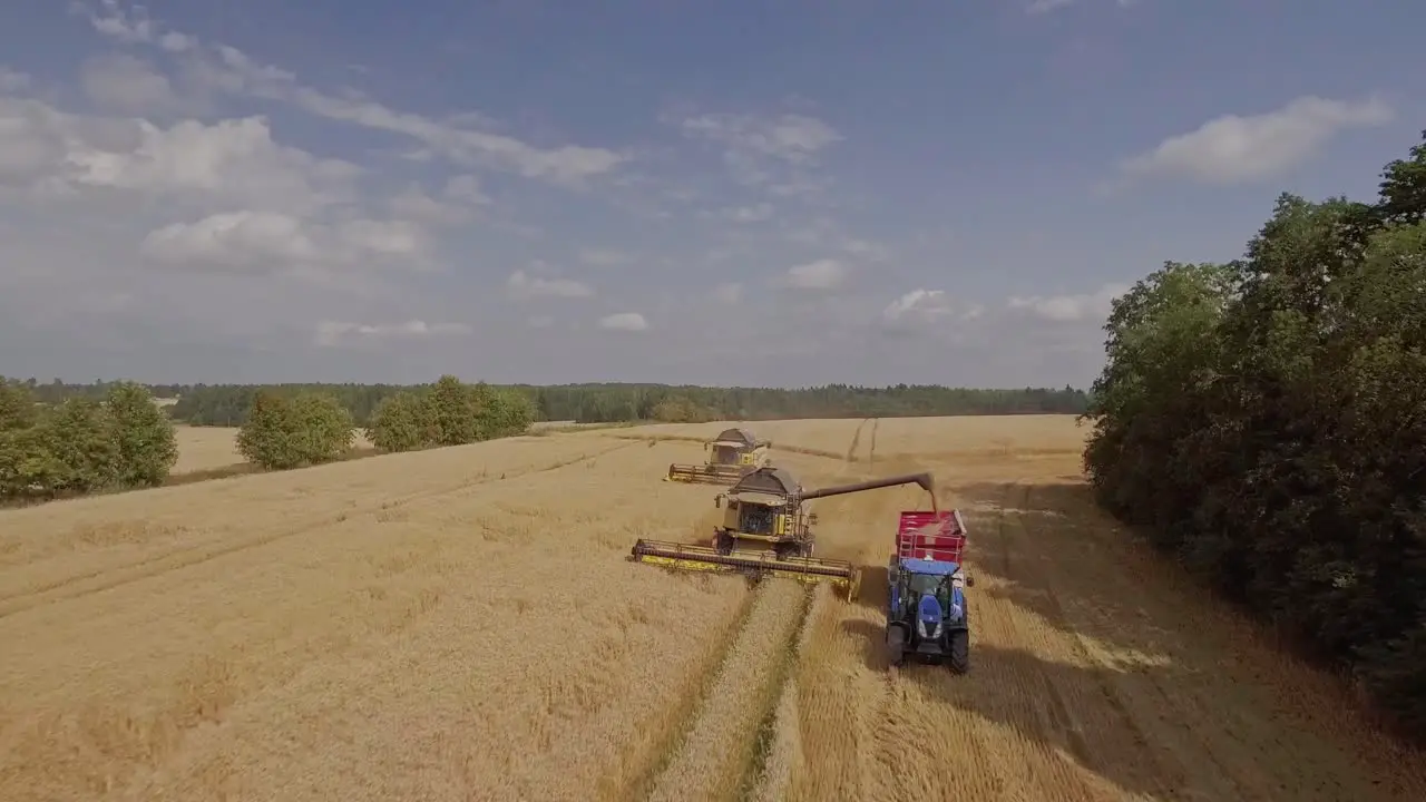 Birdseye view of a combine harvester unloading wheat onto a tractor trailer on a wheat field during harvest season