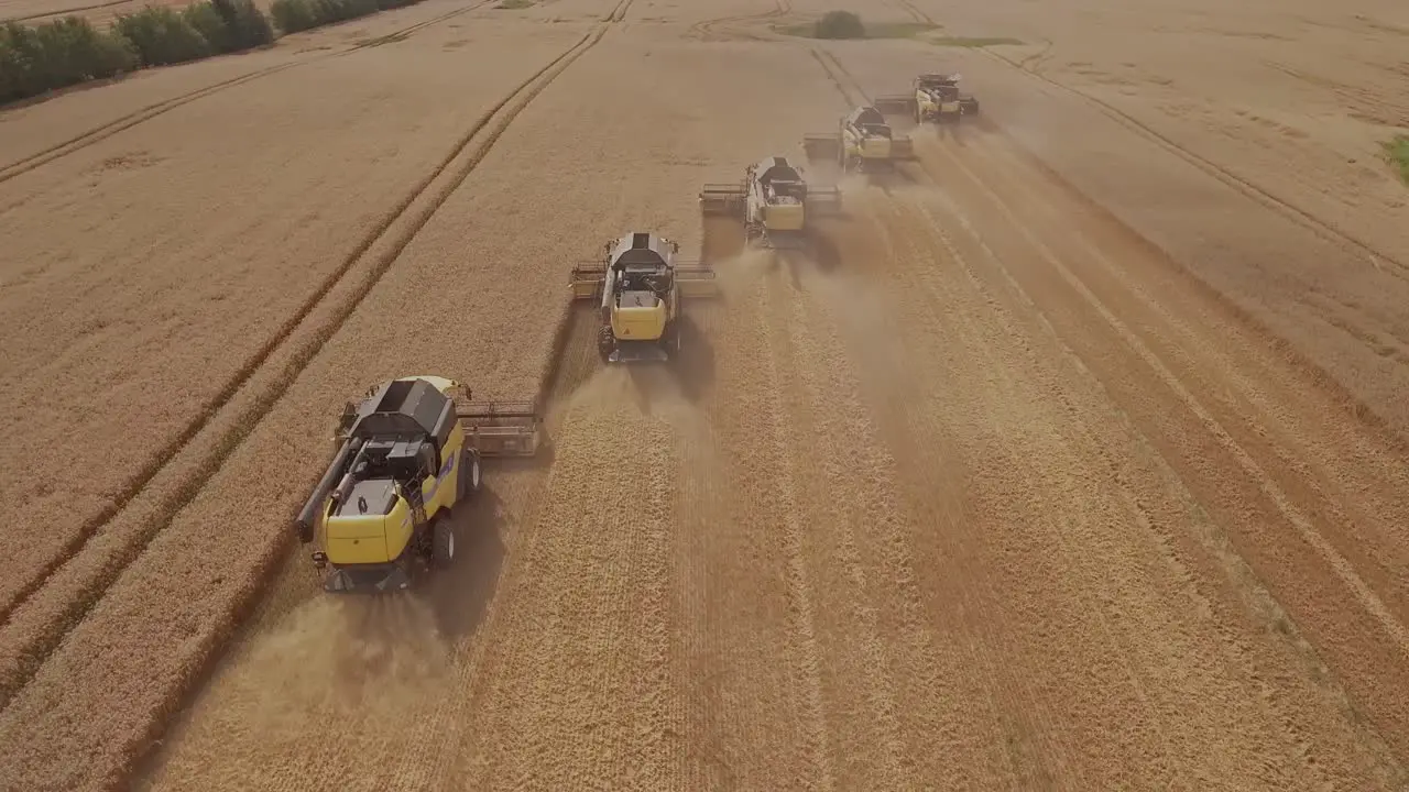 Aerial shot of a group of combine harvesters collecting wheat during harvest season and kicking up dust during the process