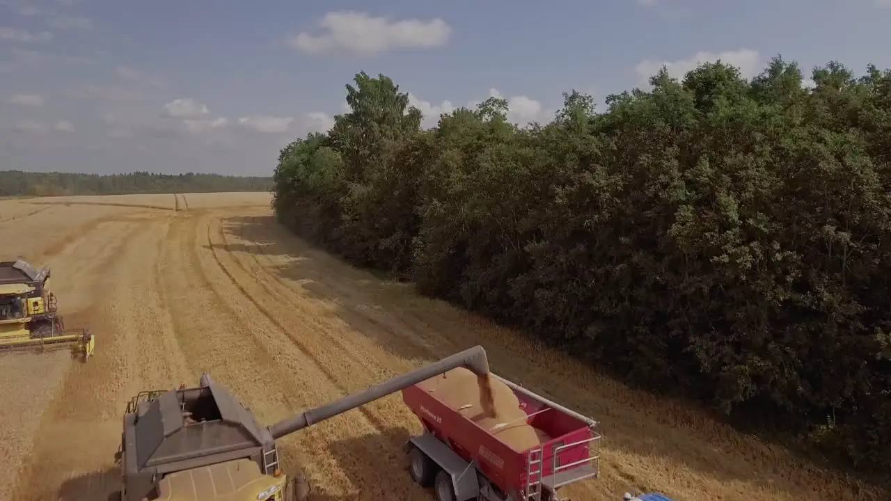 Aerial view of a combine harvester unloading wheat onto a tractor trailer on a wheat field