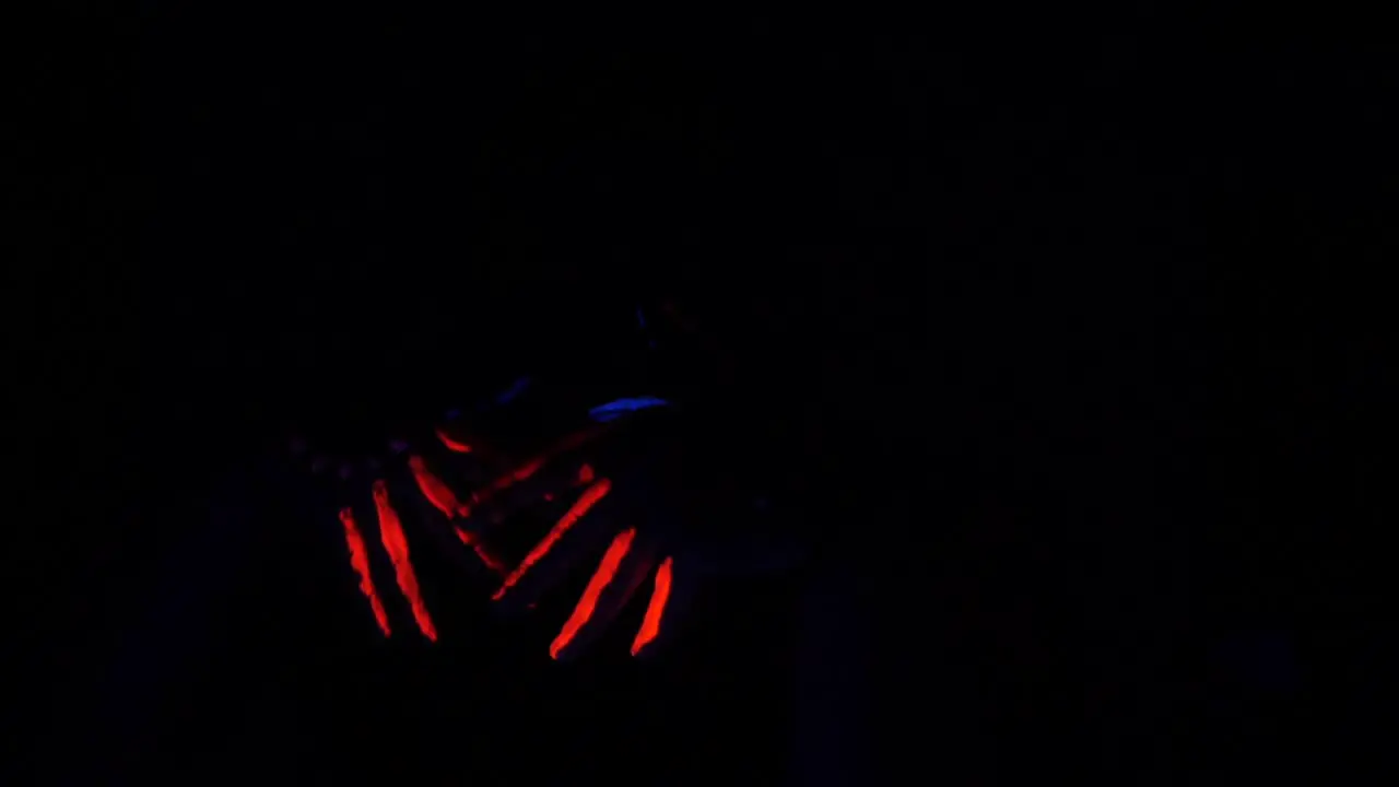 Girl plays with the motion of her hands while having glow in the dark paint on her hands and lips creating an art show in total darkness which causes an illusional effect on the perspective