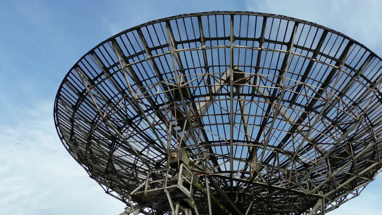 Low angle aerial view orbiting under Mullard radio telescope MRAO dish and blue sky Cambridge