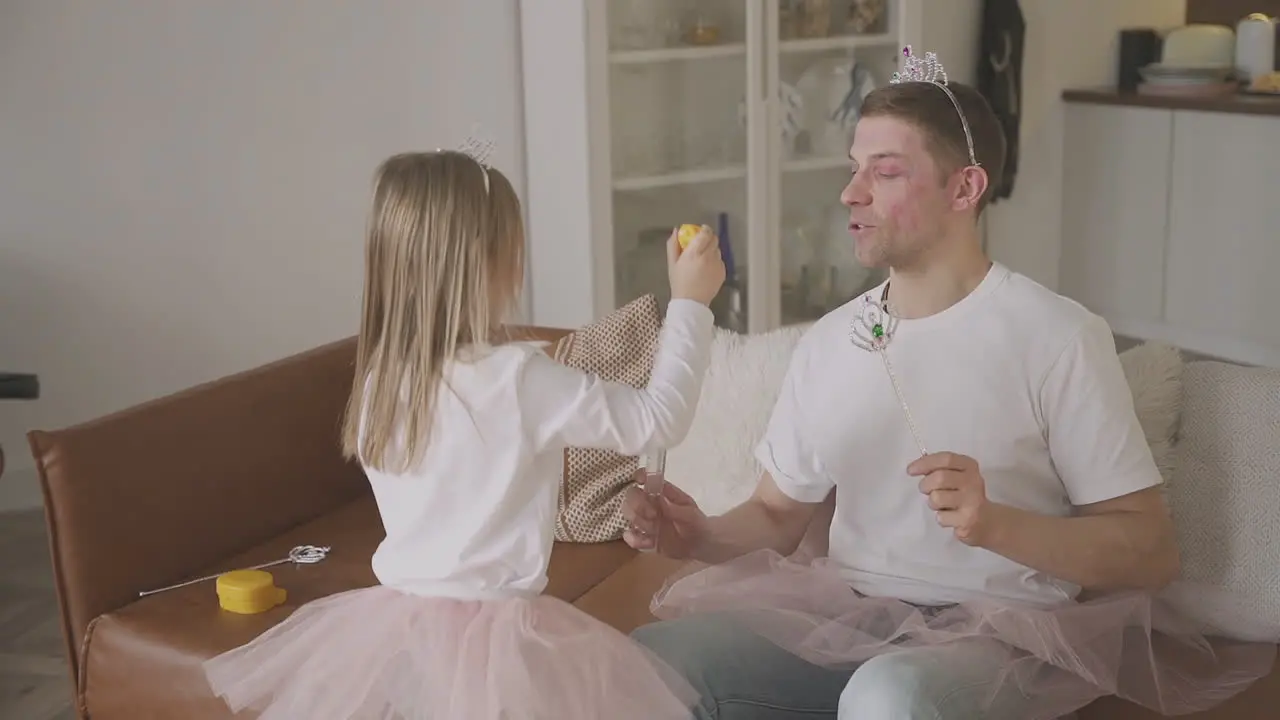 Little Daughter And Her Father Playing With Bubbles Dressed As Princesses And Fairies At Home