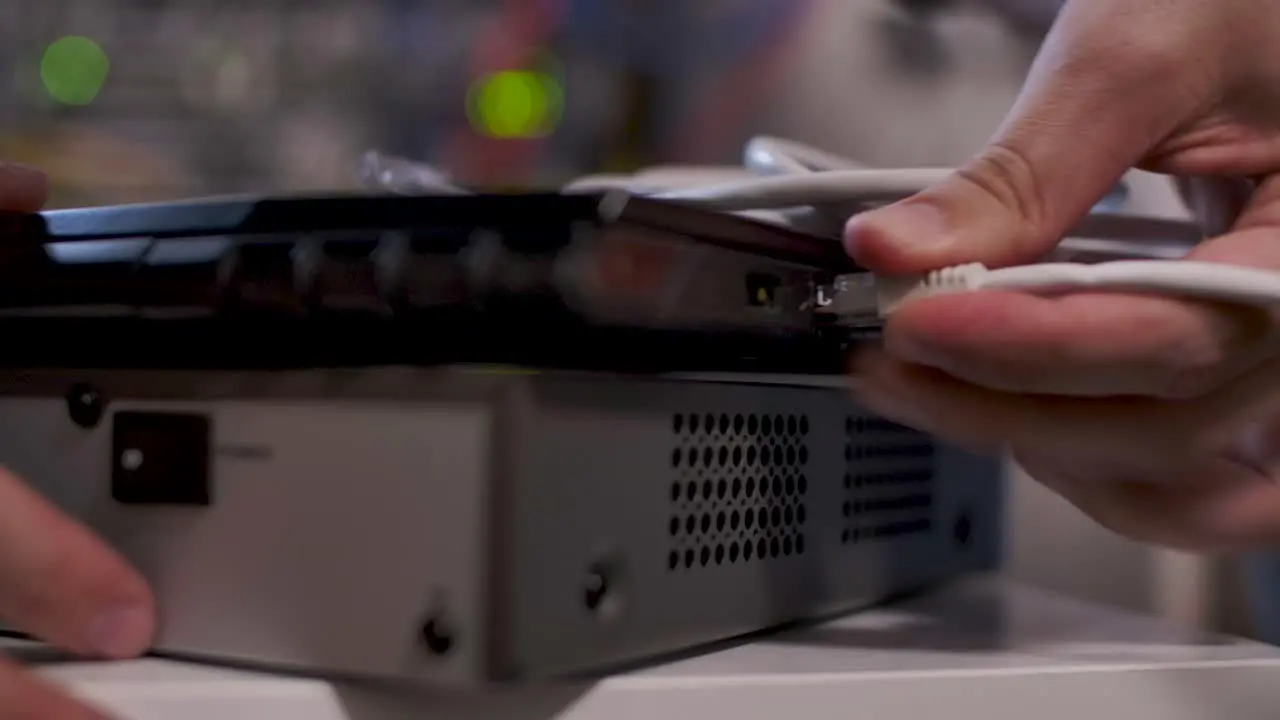 A technician inside the server room inserts a cable into the LAN port of a laptop on top of a router