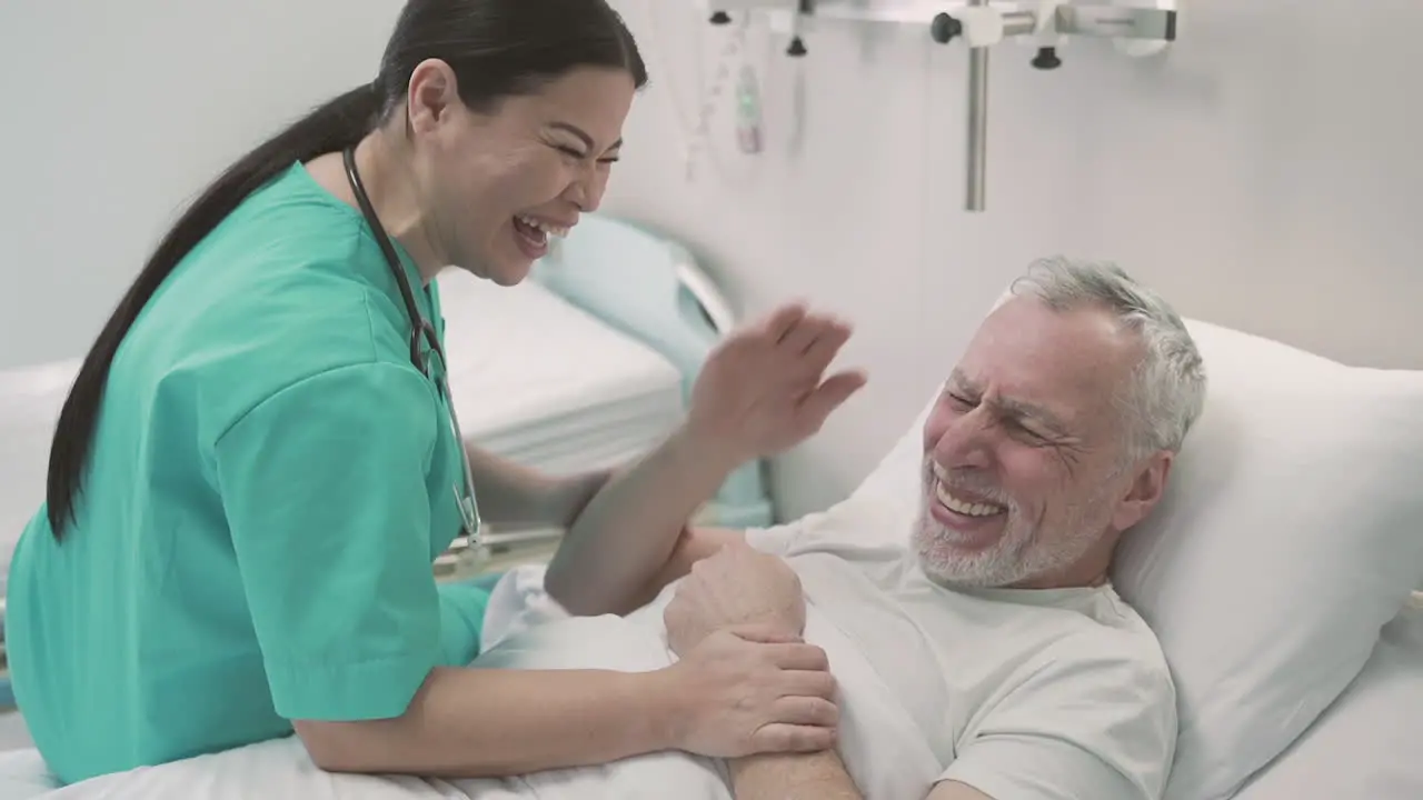 An Woman Nurse Having Fun With A Patient Who Lies On A Hospital Bed