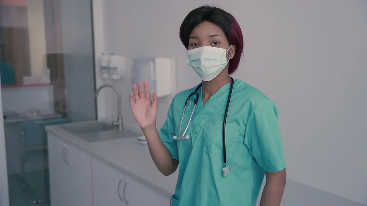 Young Female Doctor With A Facemask Says Hello To The Camera