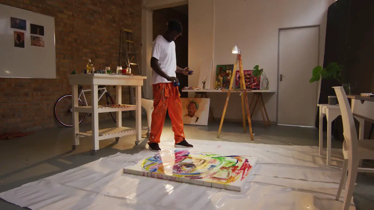 African american male artist pouring paint on canvas at art studio