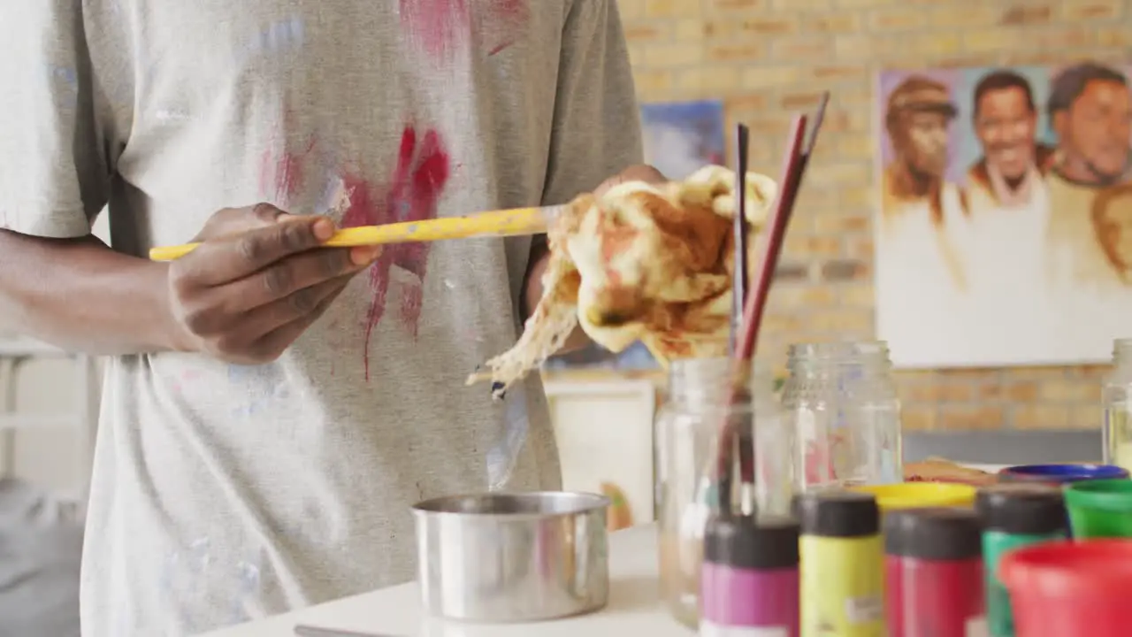 Mid section of african american male artist cleaning his paint brushes at art studio