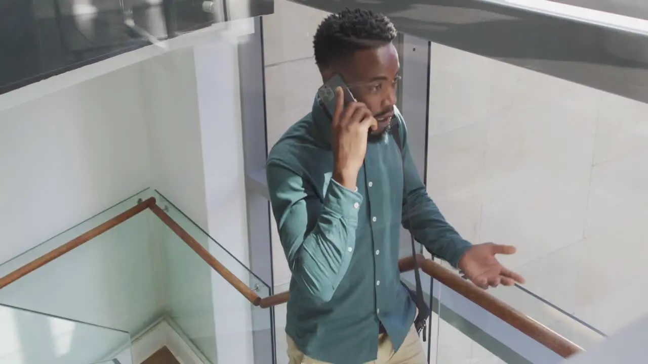 African american businessman talking on smartphone and walking in creative office