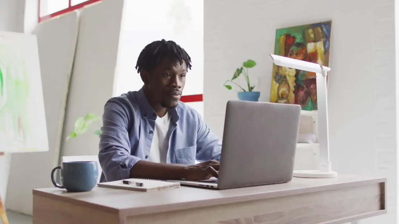 Thoughtful african american male artist using laptop while sitting on his desk at art studio