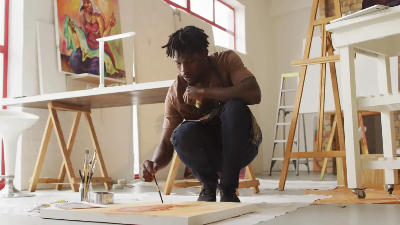 African american male artist wearing apron painting on canvas at art studio