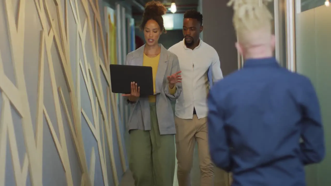 Diverse business people discussing with laptop and walking in creative office