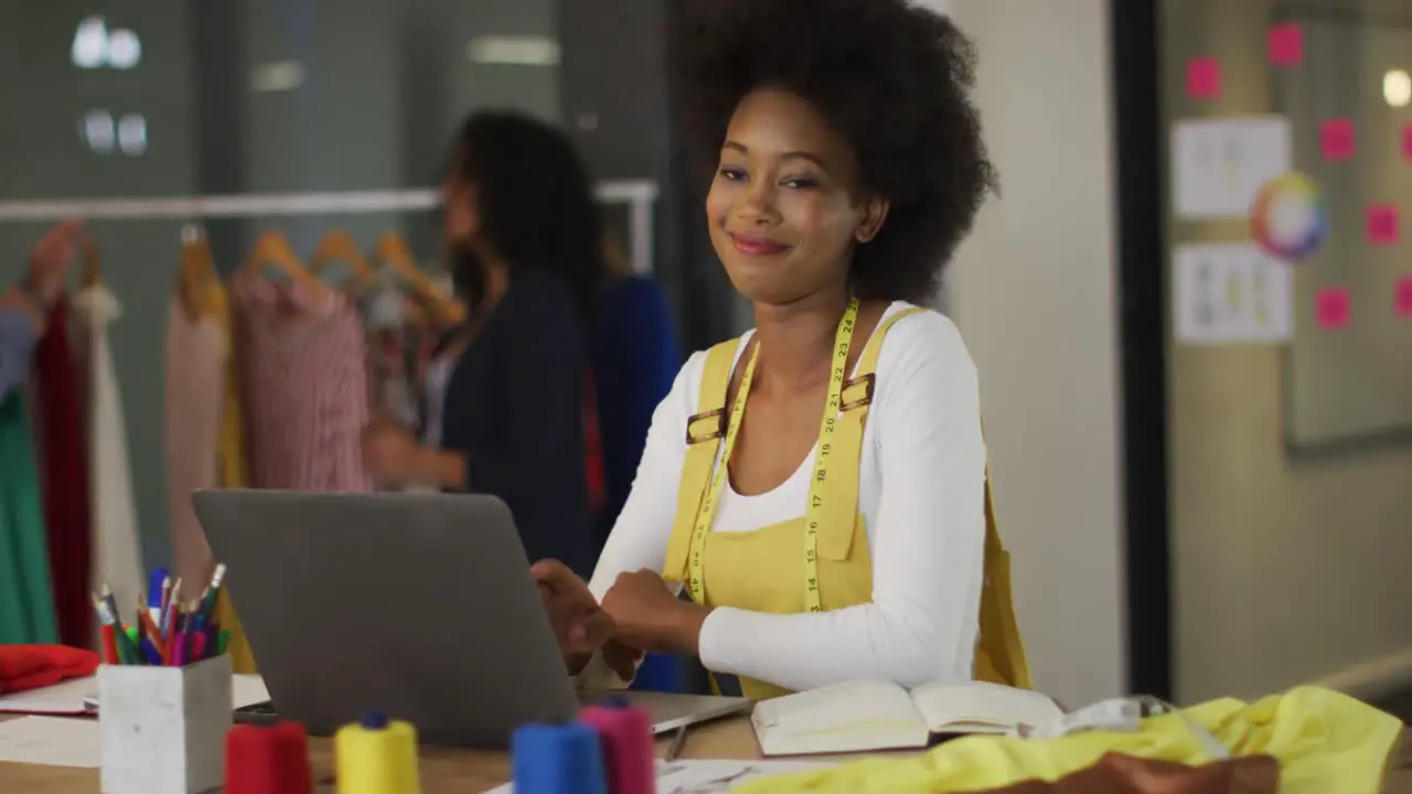 Happy african american designer sitting in front of computer smiling with colleagues in background