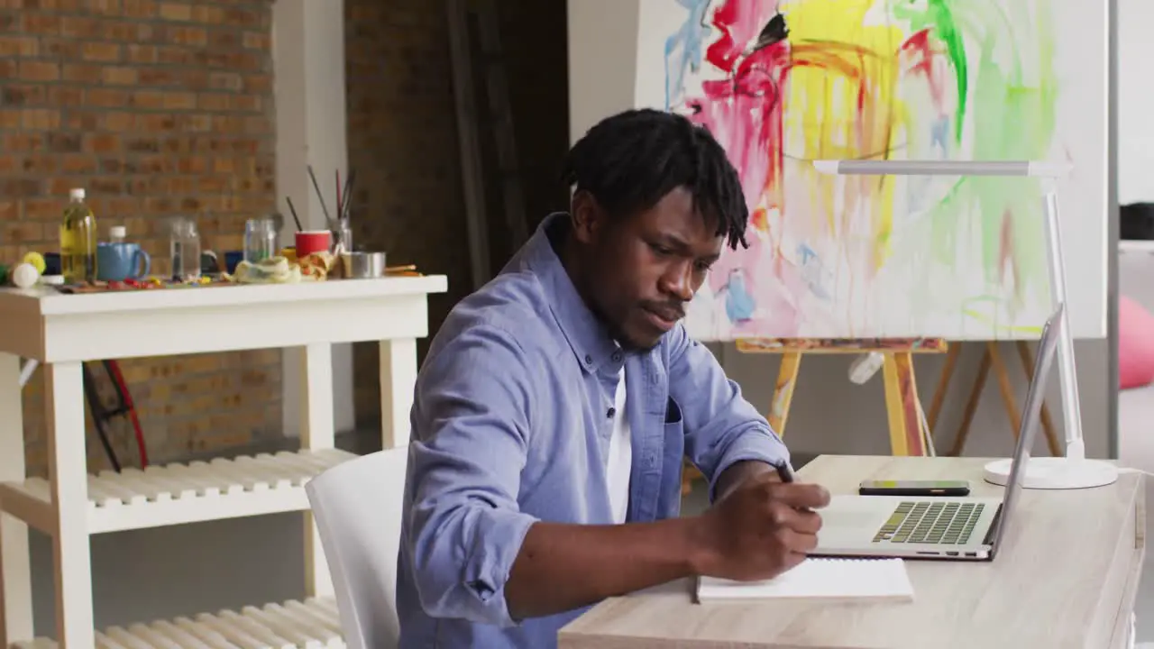 African american male artist taking notes while sitting on his desk at art studio