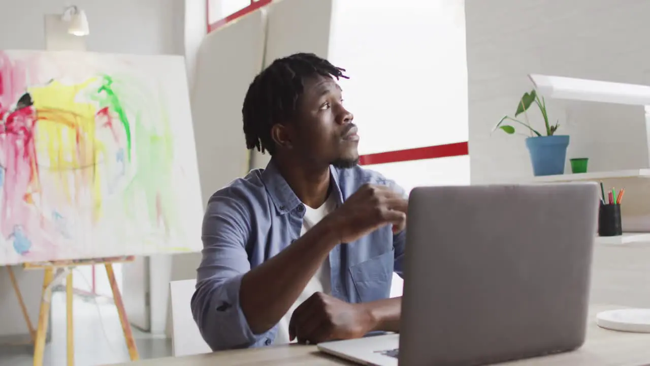 Thoughtful african american male artist with laptop sitting on his desk at art studio