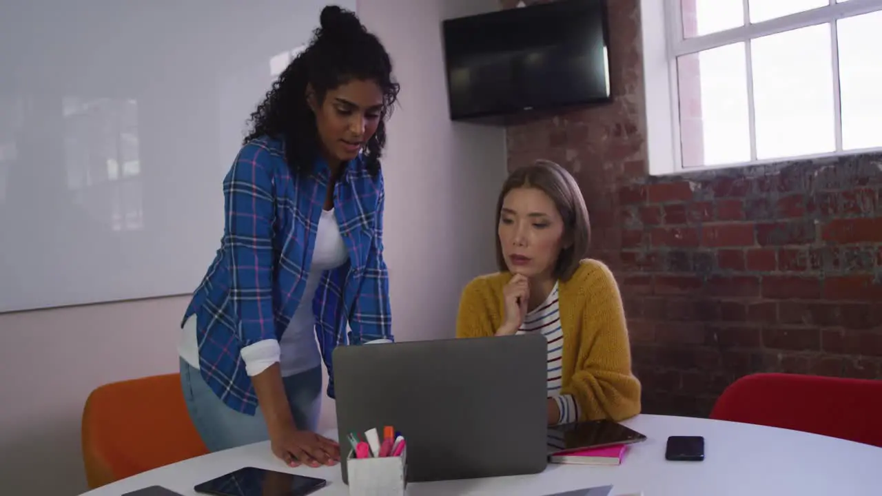 Diverse female business colleagues in discussion at work looking at laptop