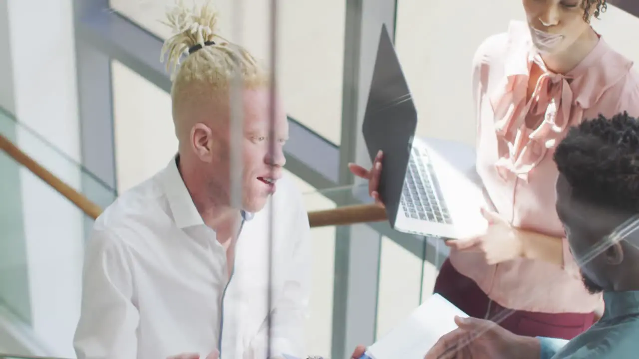 Smiling diverse business people discussing with laptop and documents in creative office