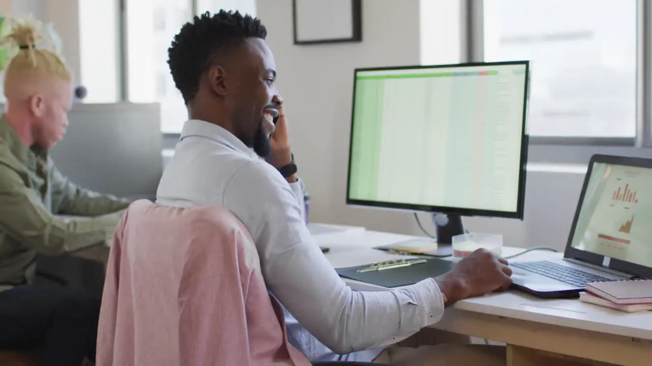 Happy african american businessman talking on smartphone in creative office