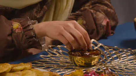 Young Muslim Woman Sitting Around Table At Home Drinking Water And Eating Dates Celebrating Eid