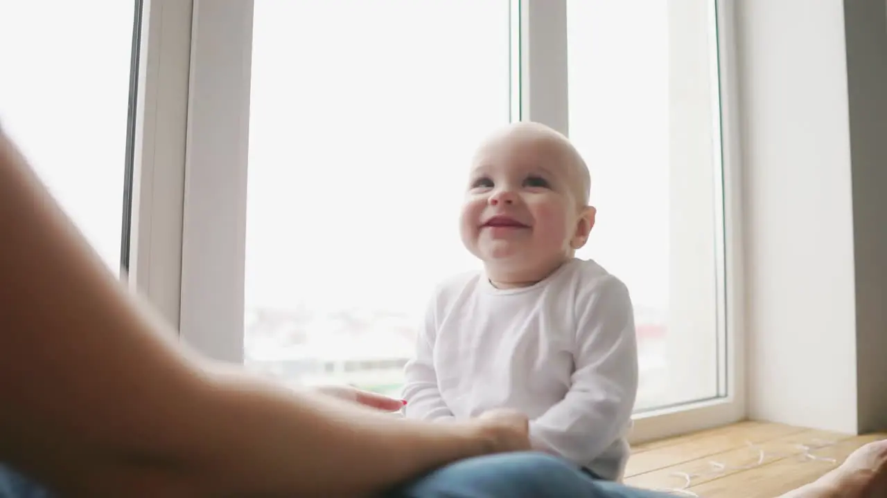 Mother and her baby son having fun and playing at home Little kid 1 years old play with his mom arms at home near a big window