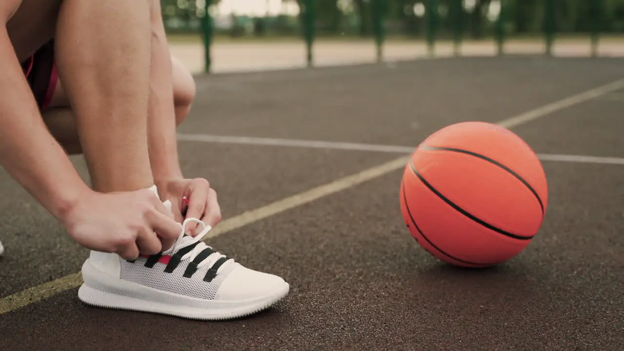 Close Up Of A Male Basketball Player Putting On His Shoe Tying Shoeslaces And Then Picking The Ball Up From The Floor In An Outdoor Basketball Court