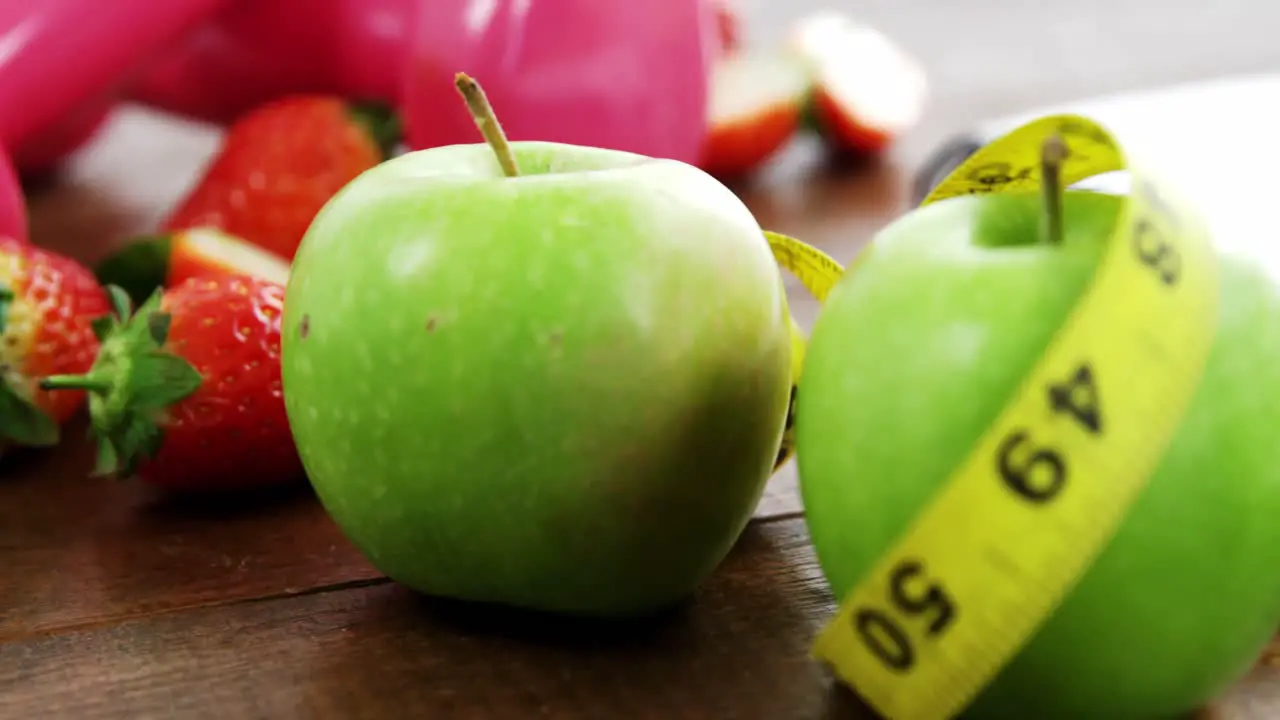 Dumbbells and fruits with measurement tape on wooden table