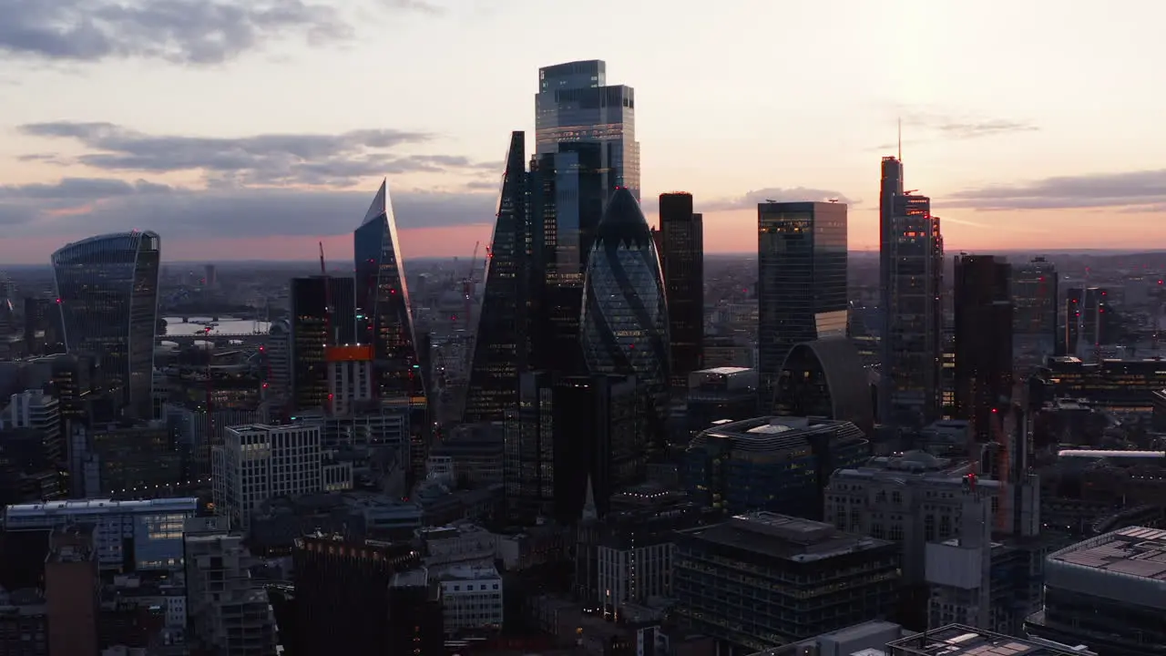 Slide and pan elevated footage of group of modern tall office buildings in City financial district View against twilight sky London UK