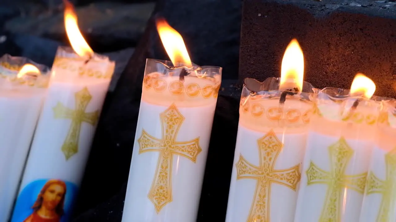 Religious wax candles burning flames flickering in breeze with Jesus Christ and cross symbol during church congregation