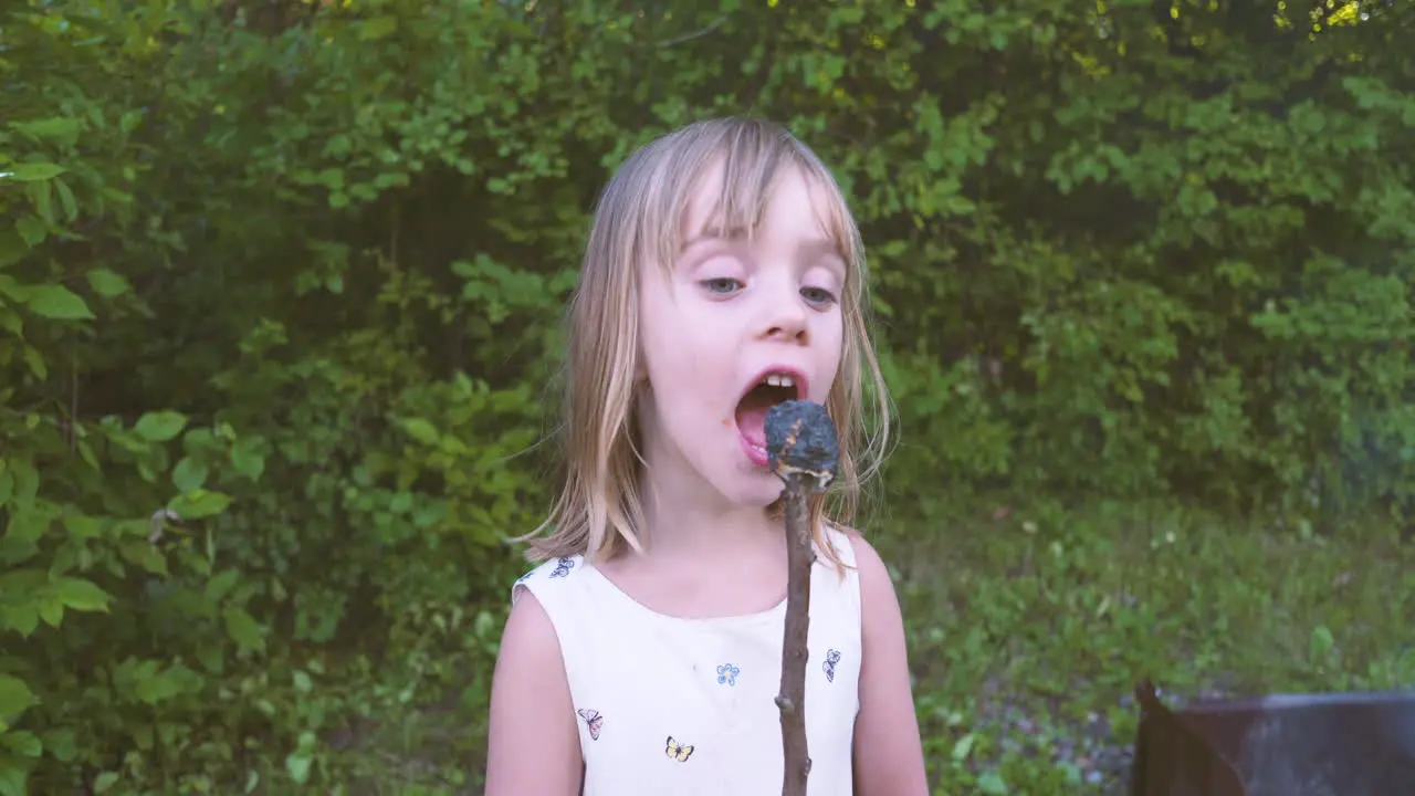 Little girl takes a bite out of a burnt marshmallow on a stick