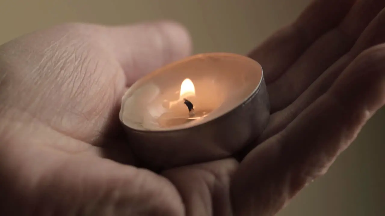 Lit tea light candle cupped in the palm of a hand