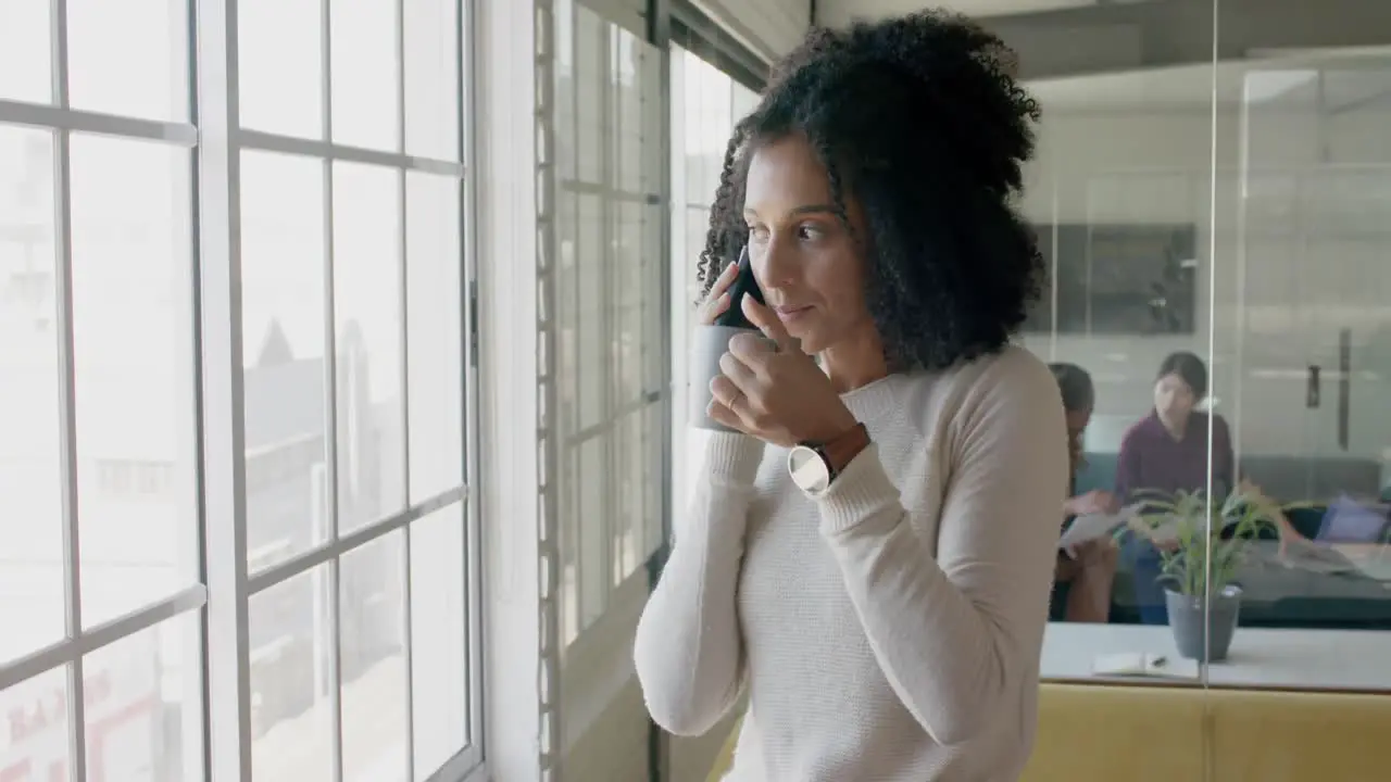 Happy biracial casual businesswoman talking on smartphone in creative office slow motion