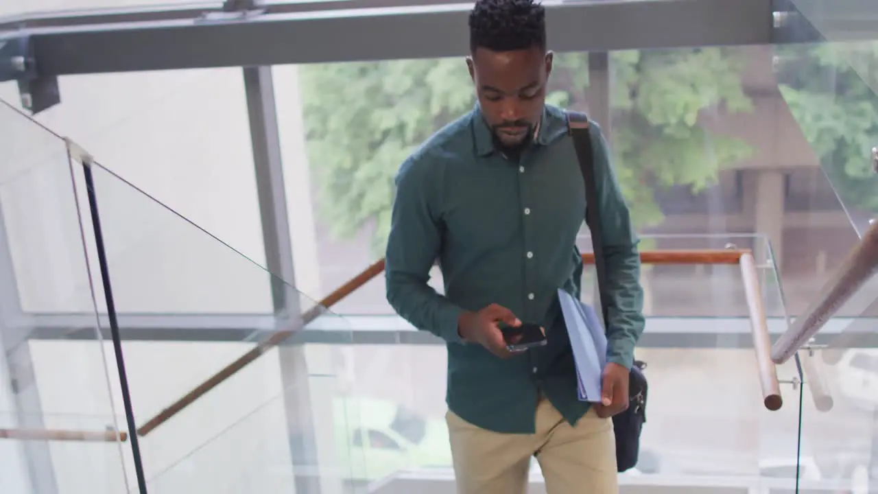 African american businessman using smartphone and holding documents in creative office